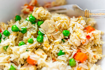 Closeup macro of homemade colorful basmati rice dish with green peas, curry and carrots with tofu and hand holding fork in bowl