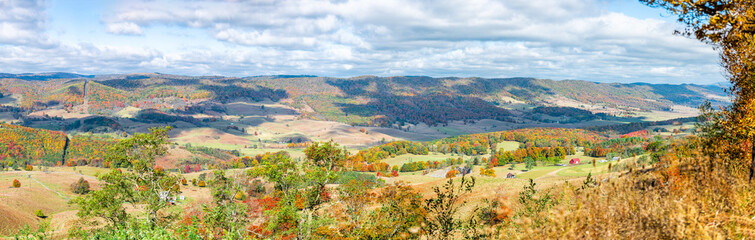 Colorful fall maple trees and panoramic farm house land rolling hills aerial above high angle view landscape panorama in Blue Grass, Highland County, Virginia
