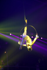 Flexible young woman make performance on aerial hoop, flexible back on aerial hoop, aerial circus show, yellow purple blue red light. Flexible woman gymnast upside down on hoop. Night club performance