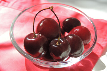 Raw fresh cherries in a glass bowl on a pink background