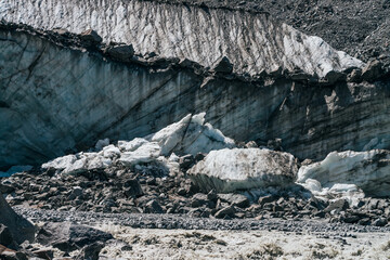 Natural texture of big glacial wall with crevasses close-up. Atmospheric nature background with ice boulders near icy broken wall with cracks. Big peace of ice and stones near surface of glacier.