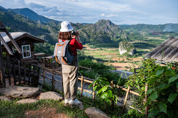 Fototapeta na wymiar Back view of young tourist woman looking to beautiful scenery view of Pha Chang Noi in Phu Langka Forest Park during green season in Phayao province of Thailand.