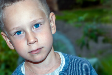 A portrait of a handsome boy of 4-5 years old with blue eyes and a serious face in the garden. A thoughtful look.Closeup