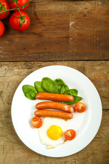 Fried egg with sausages and cherry tomatoes in a white plate on a wooden table.