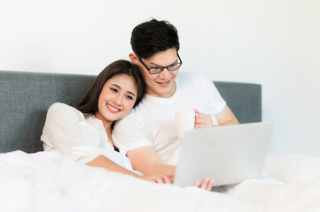 Fototapeta premium Young asian couple love man and woman watching movie in laptop on the bed in the morning. Happy moment concept.