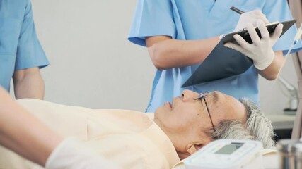 Asian medical team doctors nurse examining and checking Asian elderly male patient, health care staff take note on clipboard and pressure check with conversation in hospital.