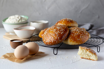 Freshly baked burger buns sprinkled with sesame seeds and ingredients on the table