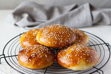 Freshly baked burger buns sprinkled with sesame seeds on baking grid