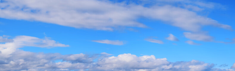 Bright blue sky with white clouds, illuminated by the sun. Beautiful summer landscape.Wide format, panorama