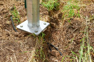 A metal support located above a narrow shallow trench dug in the ground with a thick black cable inside