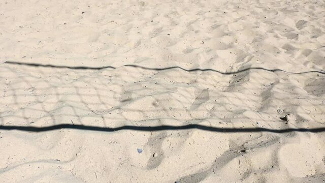 Shadow of volleyball net on sand sways in the wind. Beach volleyball court.