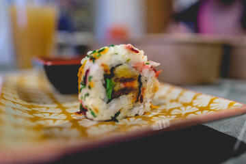 Close up of vegan sushi roll with tofu, green onion, carrot and beetroot in a plate with orange and white leaf pattern design