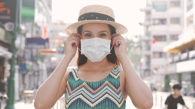 Young brunette woman traveling in Bangkok, Thailand in popular Khao San Road during Coronavirus pandemic. 20s Hispanic girl wearing a facial protective mask in summer sleeveless summer dress in Asia.