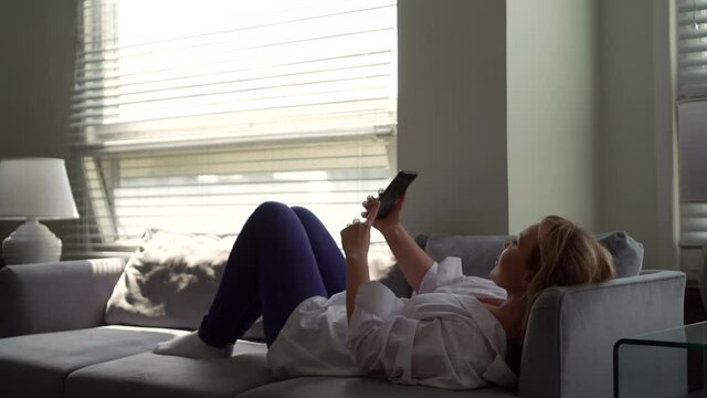 woman is photographing herself, lying on couch at home at daytime, using smartphone