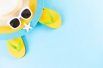 Summer or vacation concept. Beach hat, sunglasses and flip flop on light blue background. Copy...