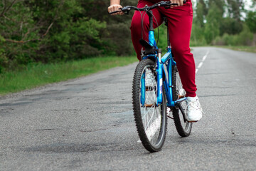 Legs on the pedals of a bicycle close-up, riding a road in the forest. The concept of a healthy lifestyle, cardio training. Copyspace.