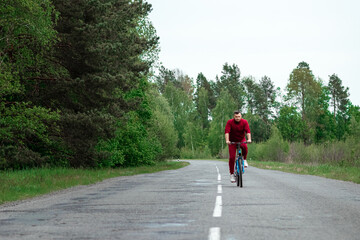 A man in a tracksuit on a bicycle rides on a road in the forest. The concept of a healthy lifestyle, cardio training. Copyspace.