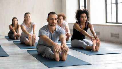 Male and female multiracial people practicing beginner yoga exercises, stretching muscles in seated...