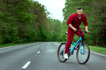 Obraz premium A man in a tracksuit on a bicycle rides on a road in the forest. The concept of a healthy lifestyle, cardio training. Copyspace.