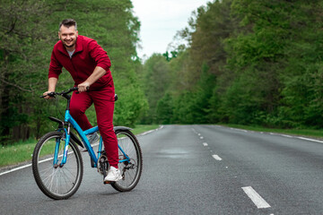 Naklejka premium A man in a tracksuit on a bicycle rides on a road in the forest. The concept of a healthy lifestyle, cardio training. Copyspace.
