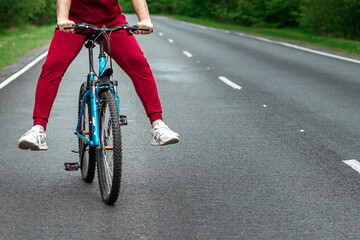 Naklejka premium Happy male riding bike with legs up. The road in the forest. The concept of a healthy lifestyle, cardio training. Copyspace.