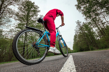 Naklejka premium A man in a tracksuit on a bicycle rides on a road in the forest. The concept of a healthy lifestyle, cardio training. Copyspace.