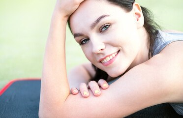 Close up happy cheerful young woman finish productive training session, lying rubber mat pleasant fatigue, smiling accomplished workout. The girl looks at the camera.