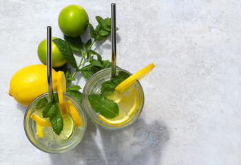 Fototapeta na wymiar Homemade refreshing summer lemonade drink with lemon, lime slices, mint, and ice cubes in glasses. Top view, copy space for text.