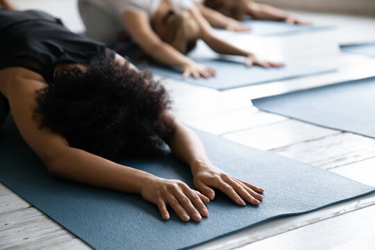 Close up focus on relaxed young african american woman lying in balasana pose on floor mat, resting after yoga group class or stretching spine back muscles in child position in modern center.