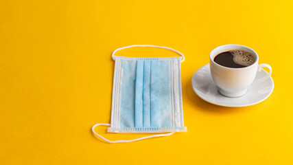 Cup of coffee and disposable face mask  on yellow backround as a symbol of new reality.