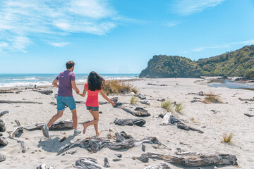 Fototapeta premium Couple walking on beach in New Zealand running having fun holding hands - young romantic couple in Ship Creek on West Coast of New Zealand. Tourist couple sightseeing South Island of New Zealand.