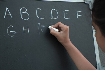 Girl writing on black board the english alphabets with chalk at her home