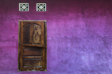 Bright purple shabby wall with closed wooden shutters window. Colorful architecture, old and vintage style. Empty place for text.