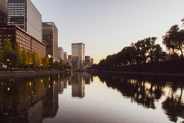 Warm Tokyo skyline and trees with reflections in still water after sunset seen from Imperial Palace Gardens.