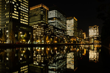 Fototapeta na wymiar Dark skyline of Tokyo city at night with illuminated buildings and reflections in the water seen from Imperial Palace Gardens.