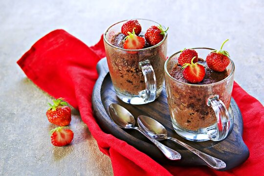 Chocolate muffin in a glass mug, decorated with fresh strawberries and mint leaves.