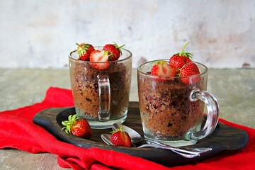 Chocolate muffin in a glass mug, decorated with fresh strawberries and mint leaves.