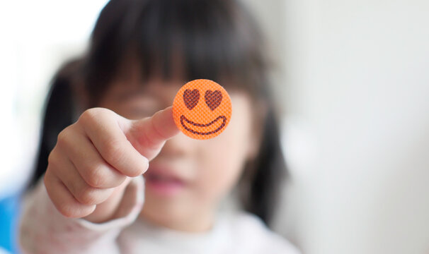 Happy little girl show smilly sticker on finger.