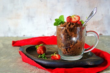 Chocolate muffin in a glass mug, decorated with fresh strawberries and mint leaves.