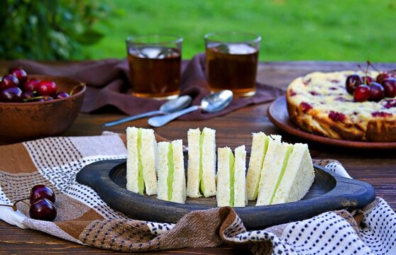 Cucumber sandwiches on a wooden plate on a brown wooden background. Afternoon tea in the garden. British cuisine.