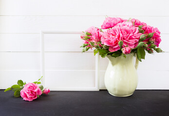 Photo frame and pink roses bouquet in vase. Empty  blank mock up, white board on background, poster product design