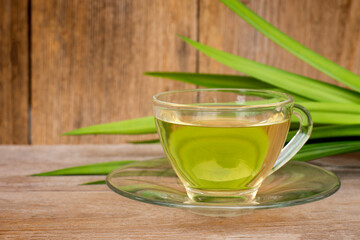 Cup glass of fresh pandan leaf ice tea or pandan juice with leaf isolated on rustic wood table background. Natural herbal plant and healthy drinks concept.