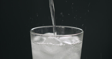 pour soda in glass with ice cubes on black background closeup