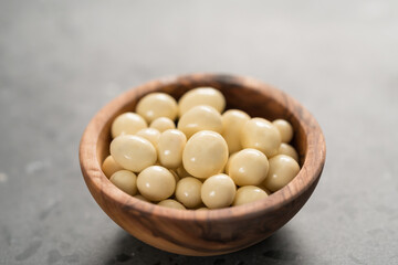 White chocolate or yogurt dragee with berries in olive wood bowl on concrete background