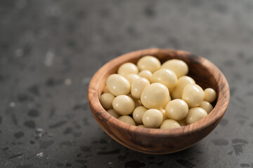 White chocolate or yogurt dragee with berries in olive wood bowl on concrete background