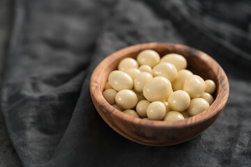 White chocolate or yogurt dragee with berries in olive wood bowl on linen background