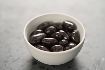 Dark chocolate dragee in white bowl on concrete background