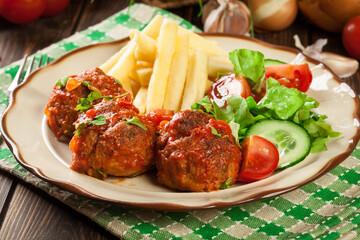 Roasted meatballs in tomato sauce with french fries and salad