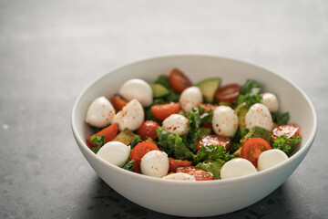 Salad with avocado, tomatoes and mozzarella in white bowl