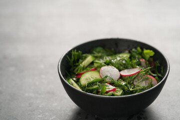 Summer fresh salad with radish, cucumber and herbs in black bowl
